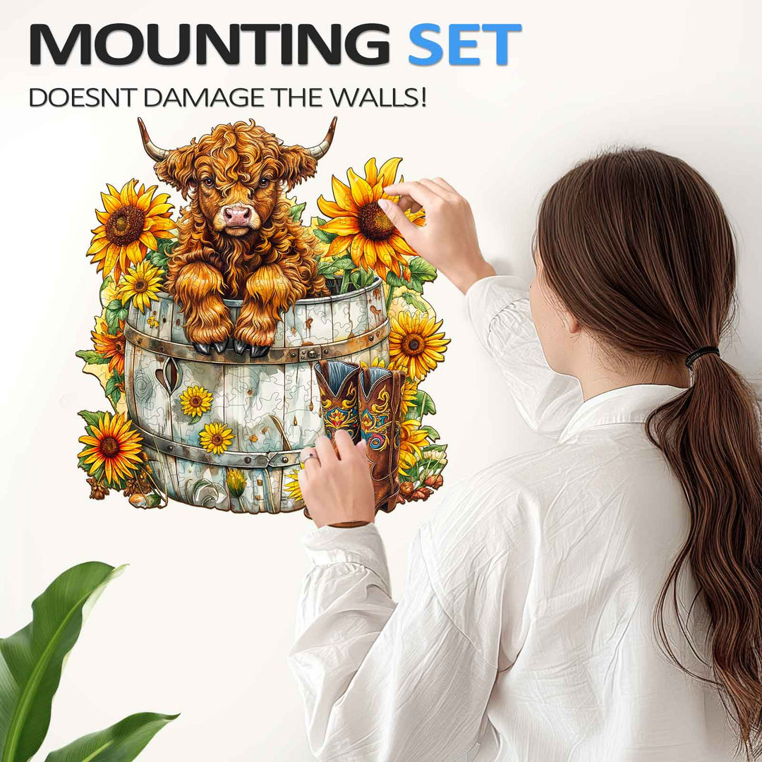 A person attaching a sunflower-themed wall art with a cow illustration, demonstrating a wall-friendly mounting set.