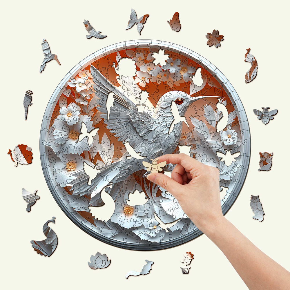 Hand placing a piece in a 3D Paper Hummingbird wooden jigsaw puzzle showcasing colorful birds and flowers.