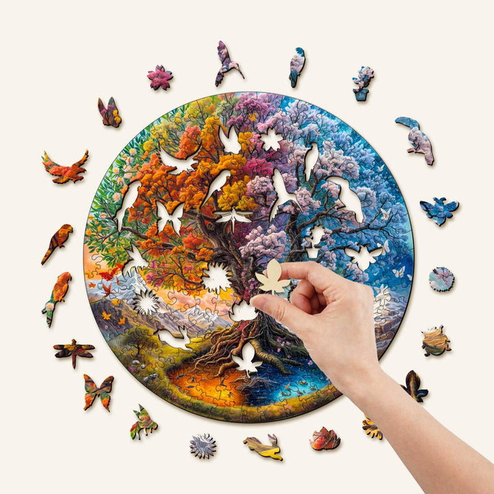 Hand placing a piece in the Seasonal Tree of Life-1 wooden jigsaw puzzle showcasing vibrant colors and unique shapes.